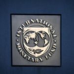 Primer plano del logotipo metálico del Fondo Monetario Internacional (FMI) sobre una pared azul, en el contexto de su advertencia sobre los impuestos a la energía.