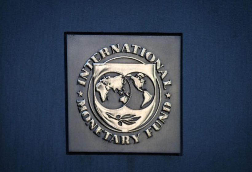 Primer plano del logotipo metálico del Fondo Monetario Internacional (FMI) sobre una pared azul, en el contexto de su advertencia sobre los impuestos a la energía.