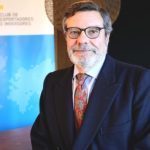 Retrato en primer plano de Antonio Bonet, presidente del Club de Exportadores e Inversores, vistiendo traje oscuro, gafas y corbata roja con motivos estampados, frente a un tótem corporativo con un mapa del mundo difuminado.