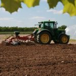 Maquinaria agrícola aplicando abono en un extenso campo de cultivo europeo, representando el impacto del precio de los fertilizantes en la producción de alimentos.