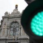 Fachada clásica del edificio del Banco de España en Madrid vista por detrás de un semáforo con la luz verde encendida y desenfocada, bajo un cielo nublado.